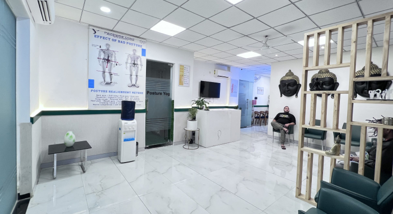 A modern physiotherapy clinic in Gurugram featuring a clean and spacious waiting area with comfortable seating. The decor includes educational posters on posture, Buddha sculptures, and a partition with plants. A patient is seated in the waiting area, creating a serene and welcoming atmosphere.