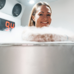 Smiling woman undergoing whole-body cryotherapy session in a cryotherapy chamber surrounded by cold mist.
