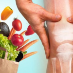 A concept image showing healthy foods like vegetables and fruits alongside a person holding their knee, with an X-ray illustration of the knee joint. This represents the connection between nutrition and joint health.