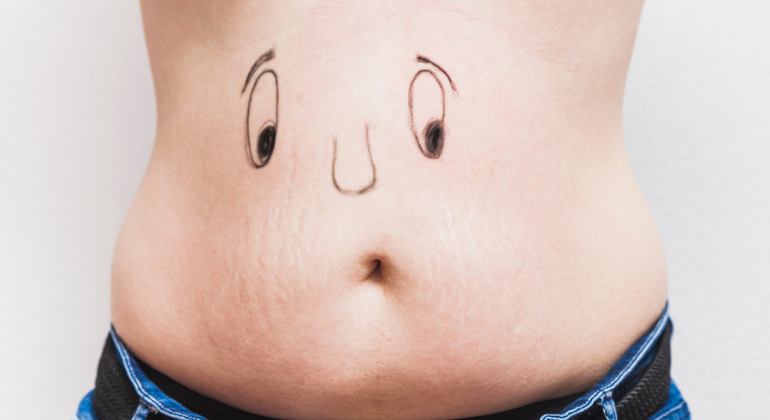 Close-up of a person's belly with a sad face drawn around the navel, symbolizing stomach discomfort, bloating, or issues like navel dislocation.
