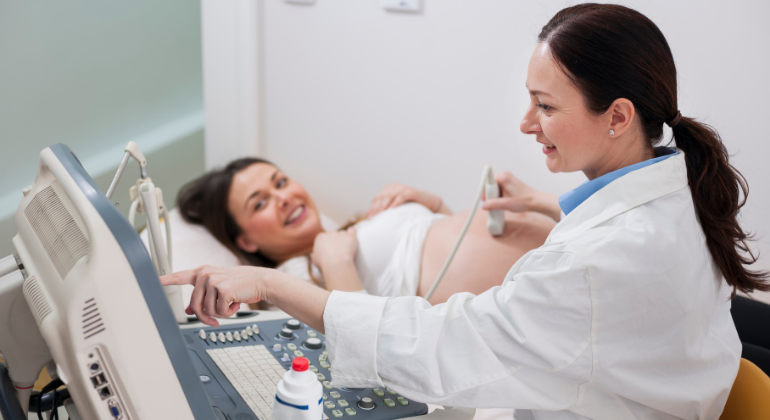 Pregnant woman lying on an examination bed smiling during an ultrasound scan, while a female doctor operates the ultrasound machine and explains the results.