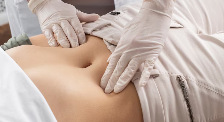 A healthcare practitioner wearing white gloves palpates a patient's lower abdomen to assess navel alignment or abdominal issues.