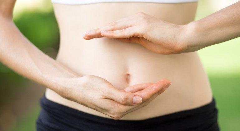 Close-up of a woman’s abdomen with hands framing the belly button, symbolizing the use of navel seed oil for digestion and wellness