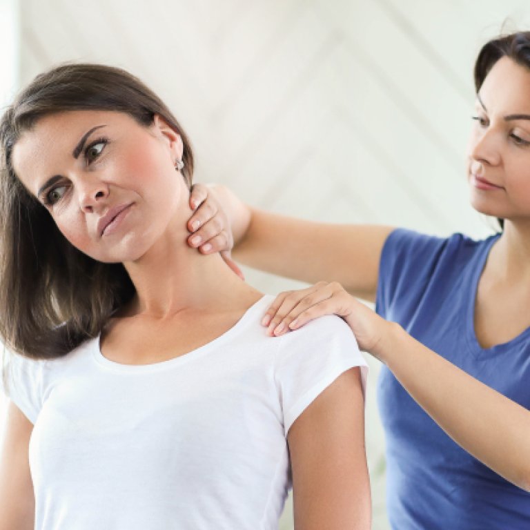 Therapist applying pressure to a patient's neck and shoulder area to relieve trigger points in a bright, modern setting