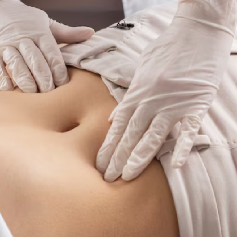 A healthcare practitioner wearing white gloves palpates a patient's lower abdomen to assess navel alignment or abdominal issues.