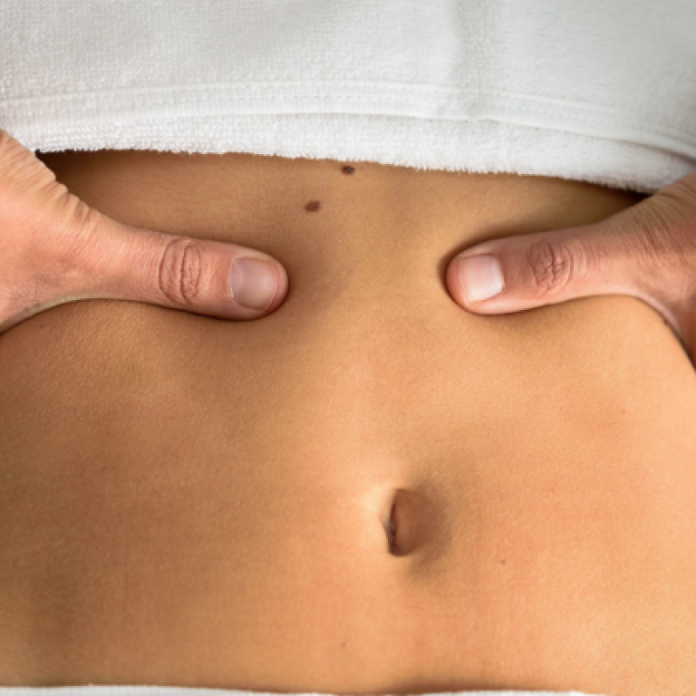 A close-up image of a person receiving an abdominal massage, with fingers applying pressure around the navel, possibly for navel realignment or relief from discomfort.