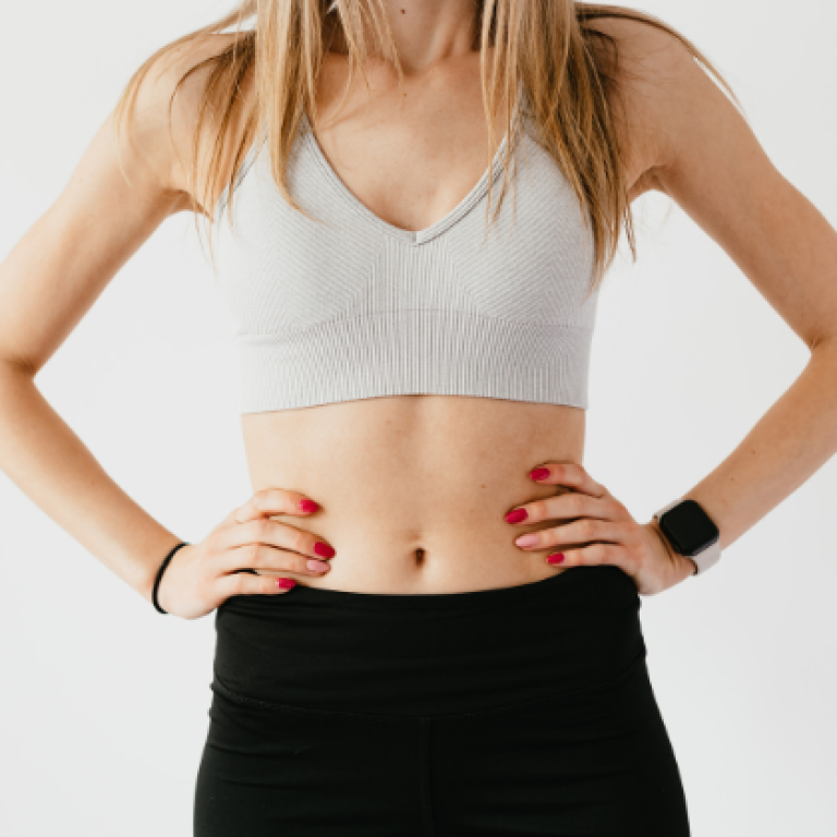 A fit woman in athletic wear standing with her hands on her waist, highlighting a strong core and abdominal area, possibly representing fitness, core strength, or digestive health.